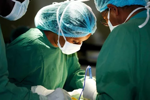 A group of surgeons operating on a patient with the spotlight on a Black female surgeon